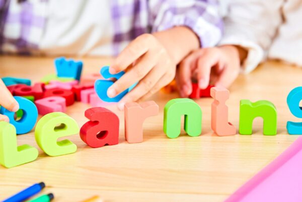 Children arranging colorful wooden letters spelling "learning" to illustrate the connection between ADHD and learning disabilities.